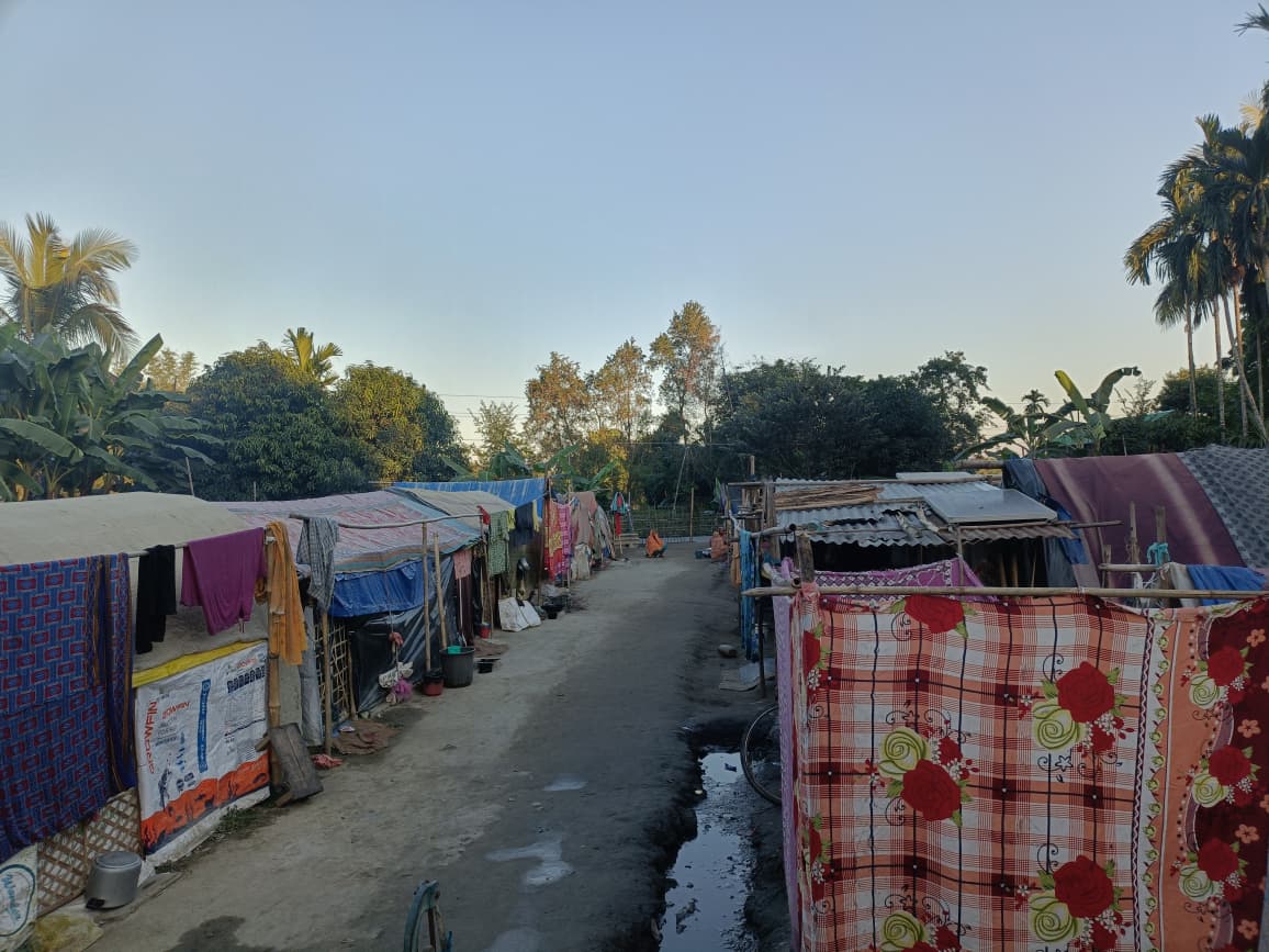 Narrow pathway between rows of tarpaulin shelters in a displacement camp
