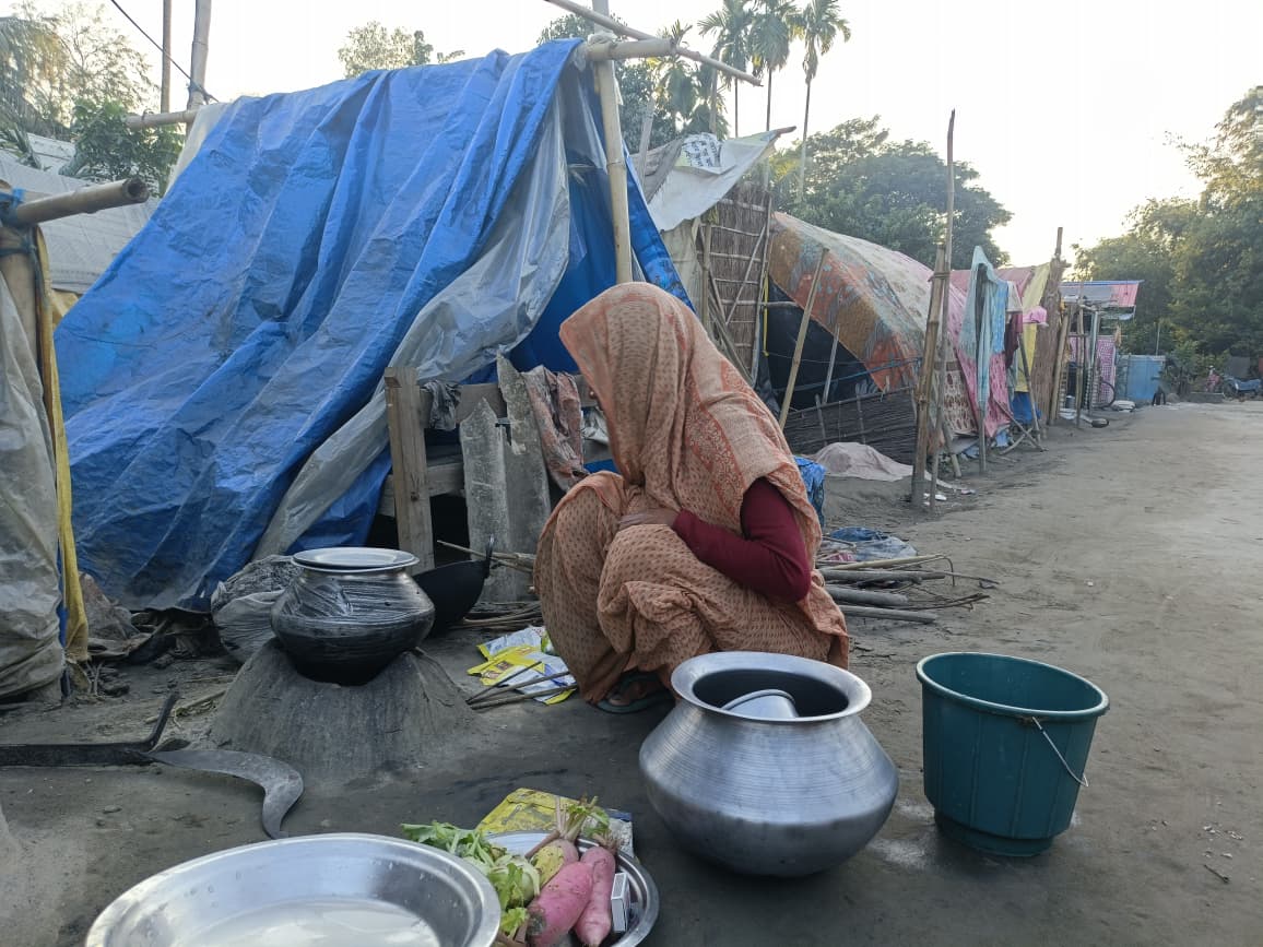 A woman prepares food outside a tarpaulin tent in a displacement camp