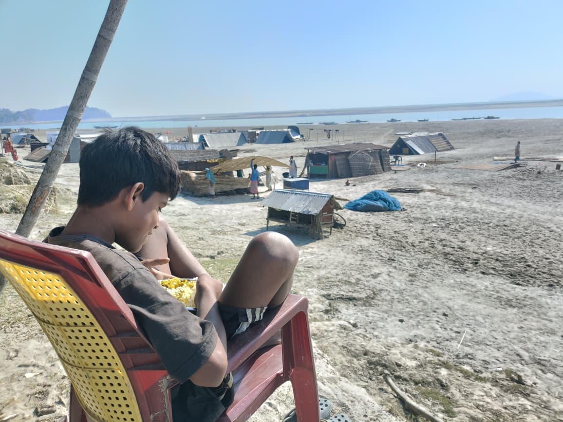 A boy eats overlooking a Brahmaputra char settlement